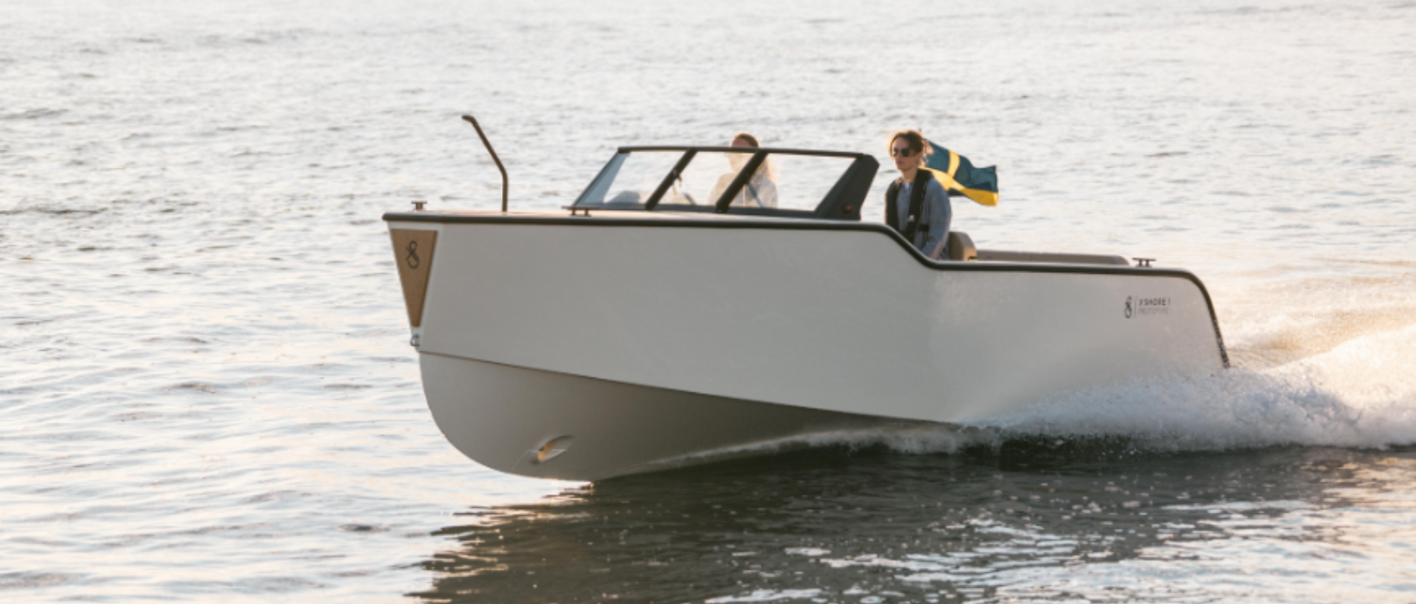 x-shore båt swishar på vattnet med 2 personer i. Svenskflagga svajar i vinden